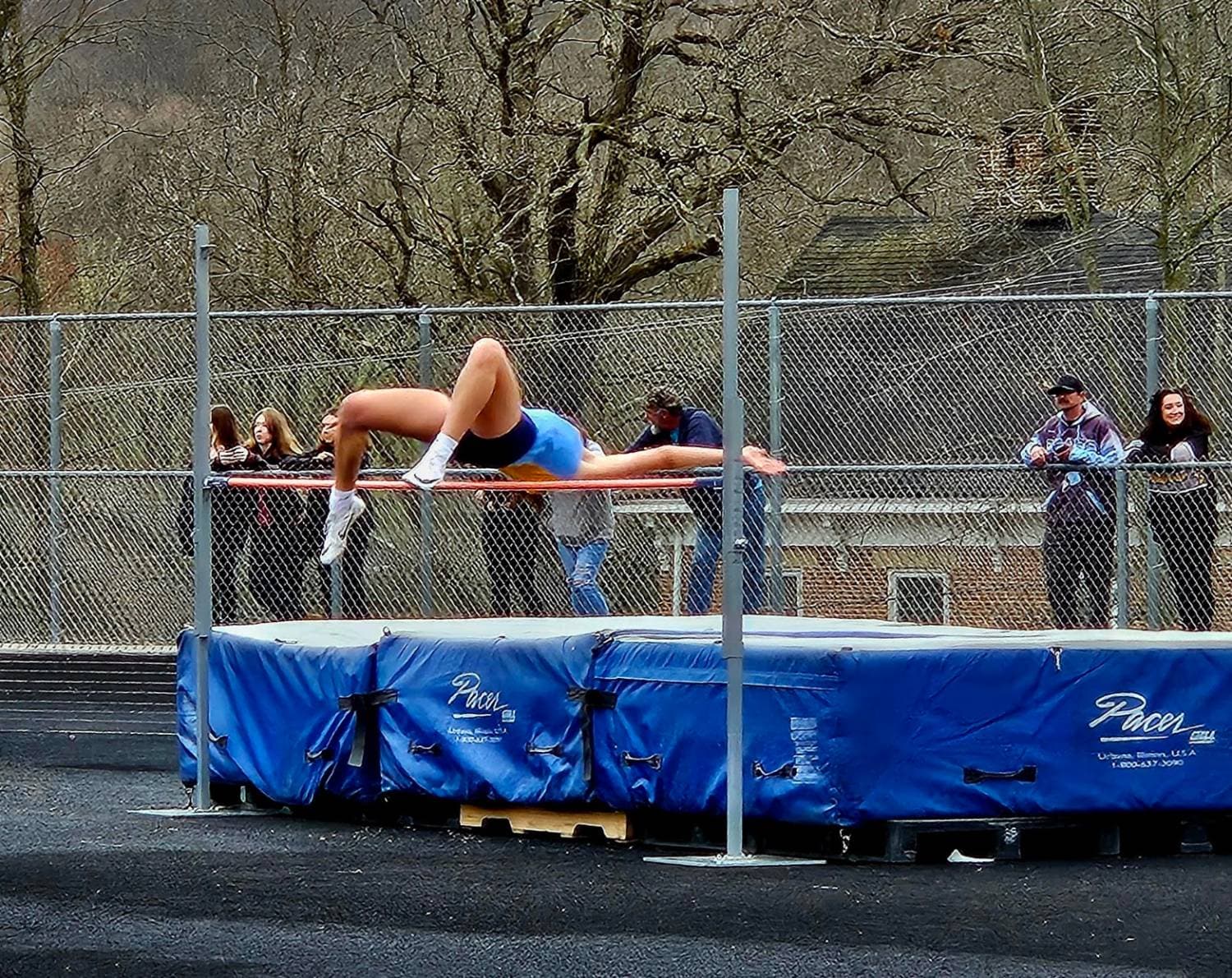 Mandy arching over the high jump bar at a track meet while people watch from the fence.