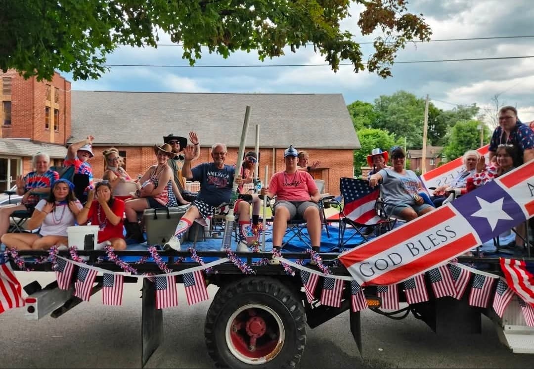 The church crew waving from a flatbed float decorated with flags and a God Bless banner.